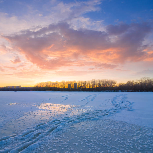 frozen winter river with forest on coast at the dramatic sunset