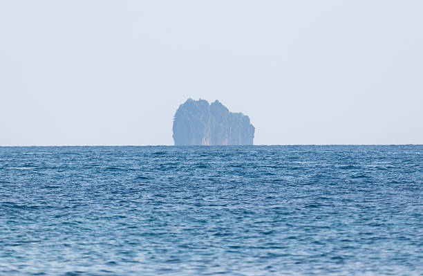 A large island is visible in the distance. The water is calm and blue. The sky is cloudy and gray