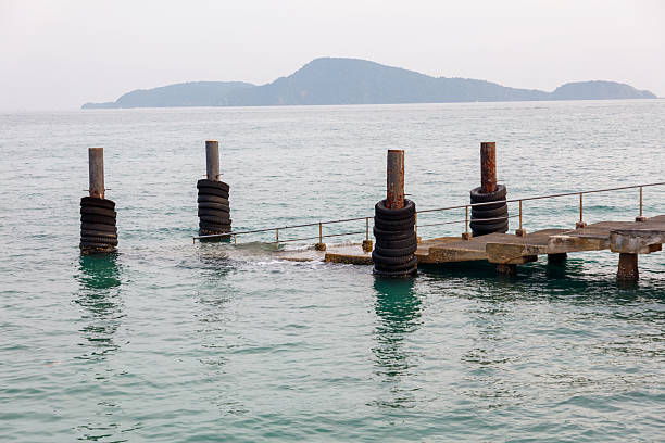 A pier with four tires on it. The pier is in the water. The water is blue