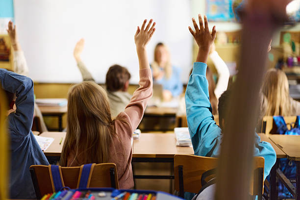 istock Back view of elementary students raising hands on a class at school. 2260192333