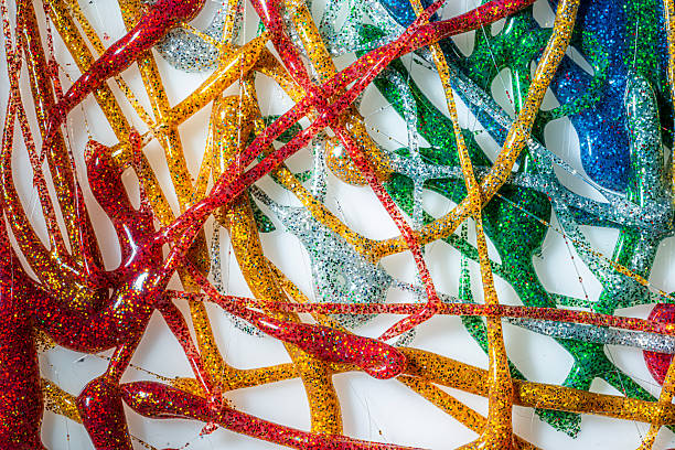Colorful glitter-coated plastic fishing lures in red, yellow, green, blue and silver overlap on a white surface, forming a dense abstract pattern with bright reflections and playful visual energy.