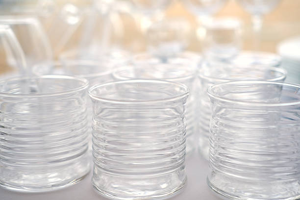 Clear glass cups with ribbed texture are arranged closely on a surface, showcasing reflections and highlights in a bright environment with soft background