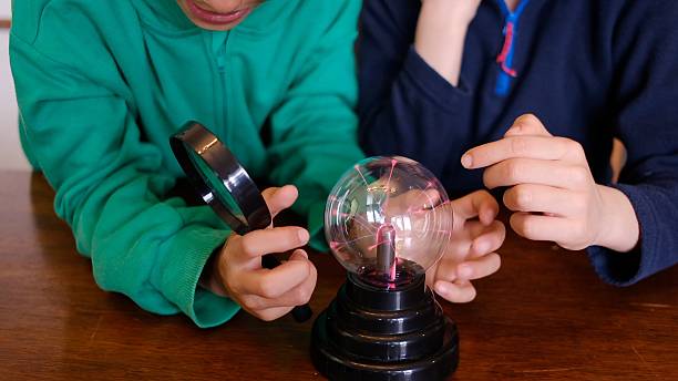 Two children actively engaging with a plasma ball using a magnifying glass, discovering the principles of electricity and science in a fun and educational home experiment