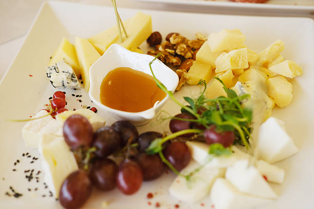 Gourmet cheese platter showcases a variety of cheeses, fresh grapes, honey, and nuts, beautifully arranged on a white plate, ideal for culinary enjoyment