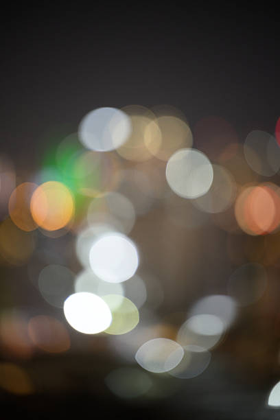 Vibrant bokeh lights create a blurred city skyline at night, showcasing a mixture of colorful circles. The soft focus emphasizes the abstract beauty of urban lighting against a dark sky, creating a serene and artistic atmosphere.