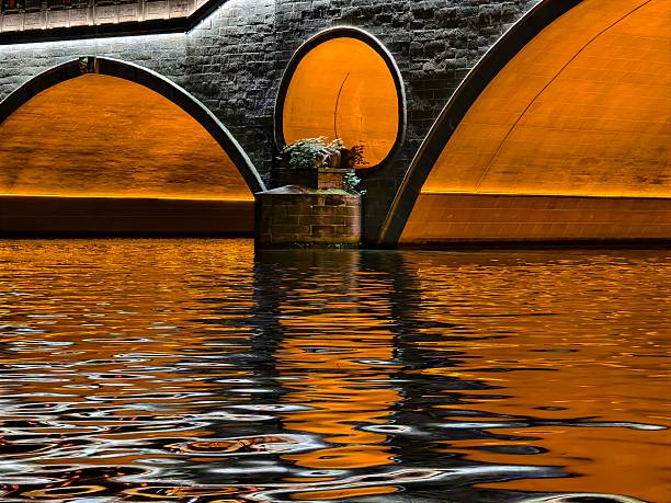 Stone bridge with arched openings reflected in water at golden hour