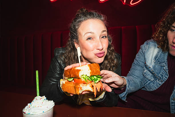 Woman holding a sandwich and sharing a moment with a friend in a retro diner