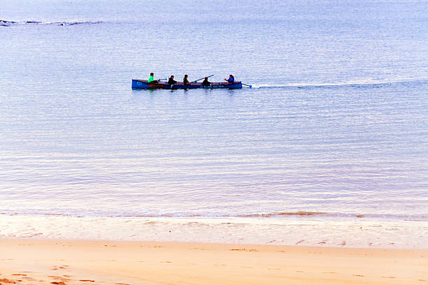 Rowing boat, young people training at dusk seen from Mera beach, sea water and sand.  A Coruña province, Galicia, Spain.