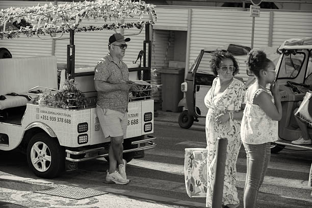 Lisbon, Portugal - August 13, 2022: A tuk-tuk driver waits for clients at a street in Lisbon downtown, while holding a menu card.
