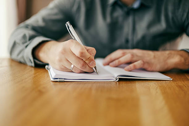 istock Person writing notes in notebook at wooden desk 2260234370