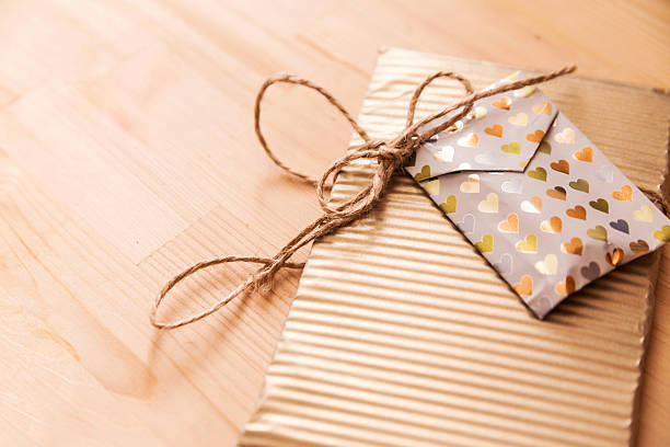 Gift package adorned with golden stripes and a heart-patterned envelope, resting on a wooden surface, creating a cozy and inviting scene with copy space