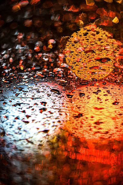 Abstract view of blurred city traffic lights seen through a rain-covered car window, creating a moody urban atmosphere at night.