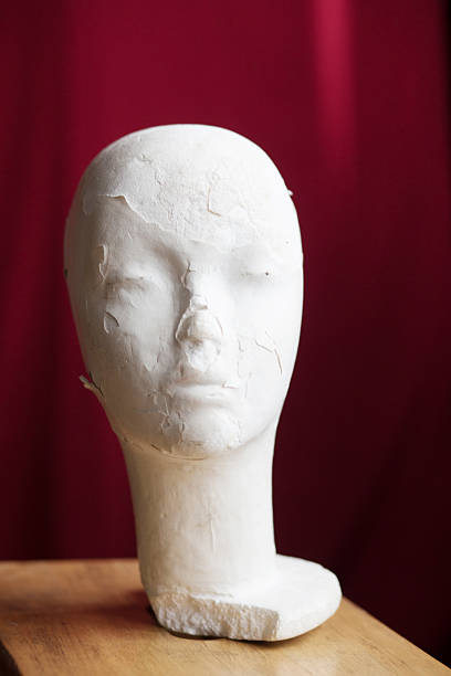Plaster mannequin head positioned on wooden table with a deep red background, highlighting unique textures and artistic qualities, perfect for creative inspiration