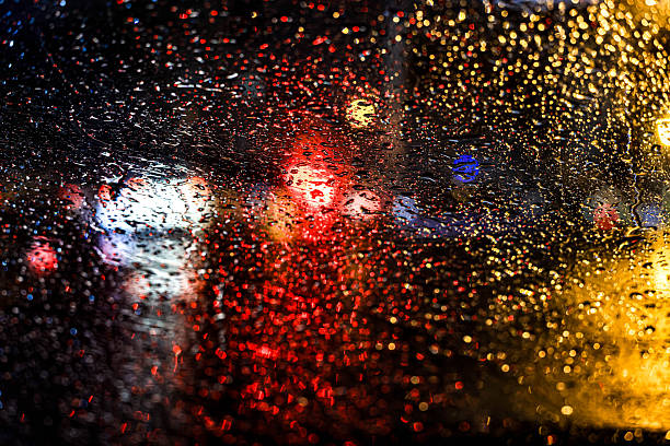 Abstract view of blurred city traffic lights seen through a rain-covered car window, creating a moody urban atmosphere at night.