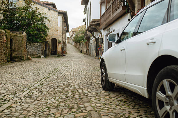 A quiet rural stone-paved street with a parked car, representing traditional village life, slow travel, countryside architecture, and everyday transportation.