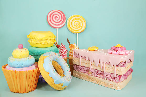 Artificial sweets made from polystyrene foam, including colorful cupcakes, macarons, donuts, and lollipops arranged on a light blue background