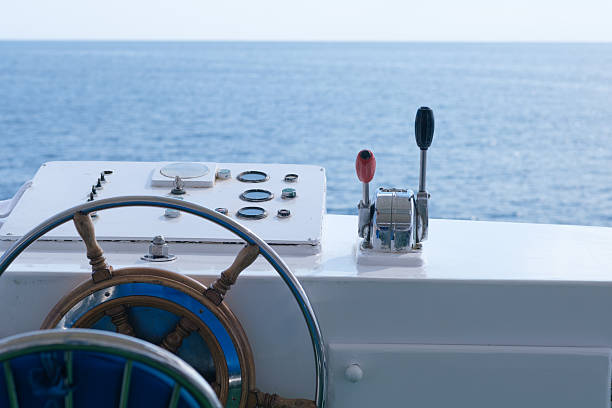 Boat steering wheel and control panel featuring gauges, positioned against a backdrop of calm ocean waters under a clear sky