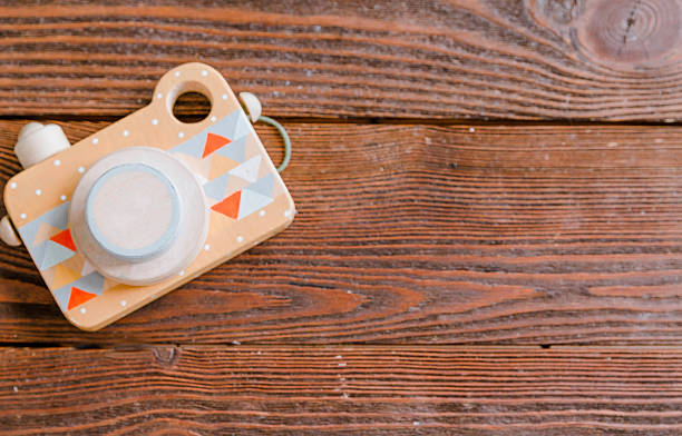 Wooden toy camera featuring geometric patterns rests on a rustic wooden surface, highlighting its playful design and craftsmanship in a natural environment