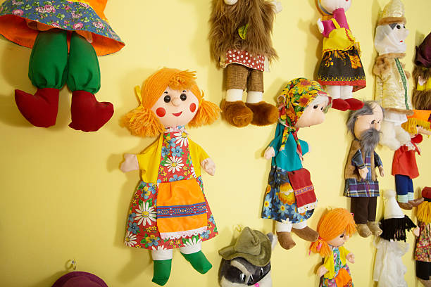 Fairytale character dolls hang on a yellow wall in a kindergarten play studio, featuring diverse outfits and bright colors for children's imaginative play