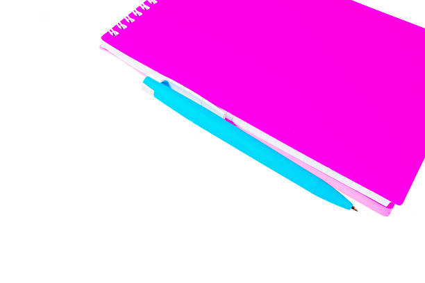Pink spiral notebook positioned next to a blue pen on a white background, highlighting the bright colors and simple design of office stationery