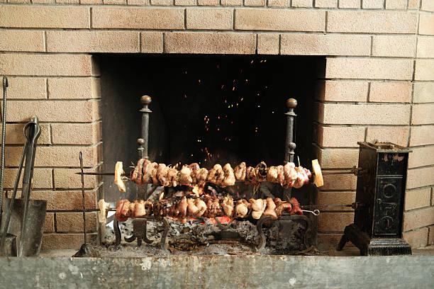 Skewers of meat rotating over glowing embers in a traditional brick fireplace for a slow cooked meal