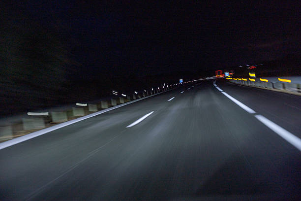 A dark road with a car driving down it. The car is in the foreground and the road is in the background