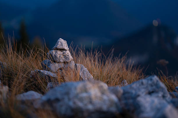 tiny heap of stones arranged in dry grass high up in the montains on cold autumn evening during blue hour, shallow focus on cairn