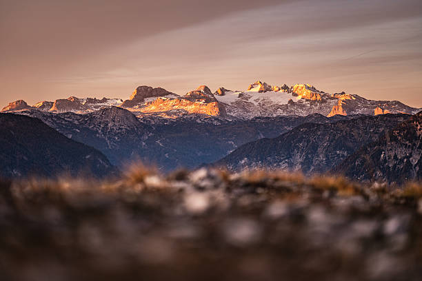 sun rising from left side starting to illuminate Dachstein mountain on cold morning in autumn, shallow focus on background, dry grass in foreground blurred