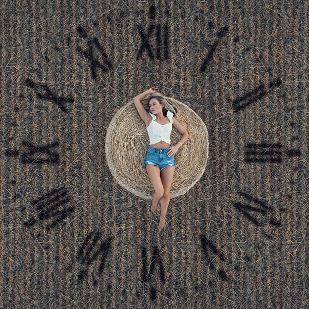 Young woman lying on a hay bale with Roman numerals in a field, symbolizing time passing