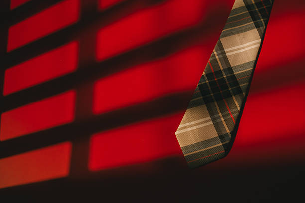 Plaid necktie hanging with red and black shadow pattern background, stylish accessory with warm lighting creating dramatic mood.