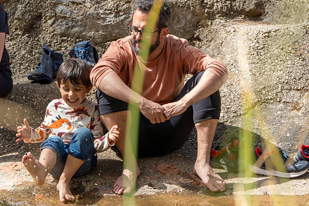 Kid with barefoot splashing in the river water with his father