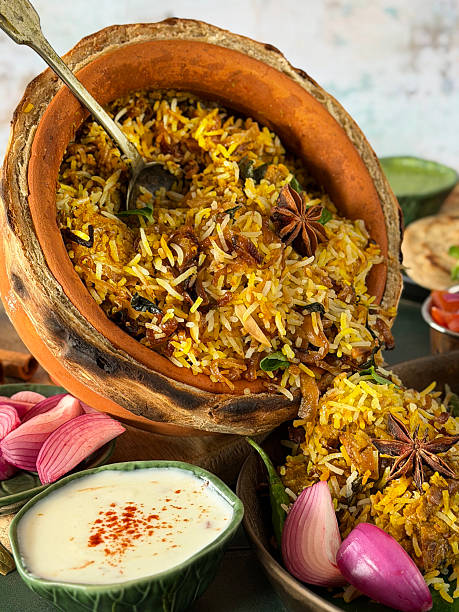 Image of Indian takeaway chicken dum biryani rice served in terracotta clay pot handi with lachha paratha, flavorful dips and chutneys