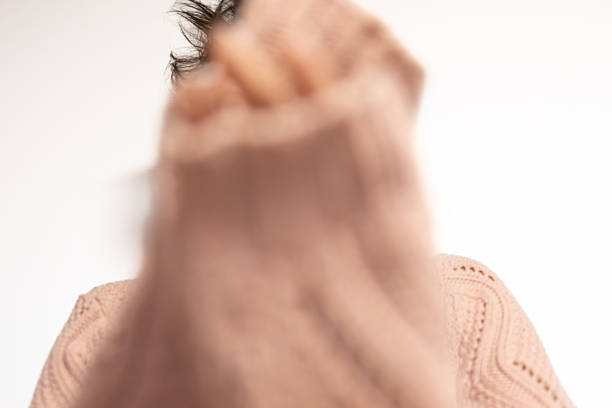 Mature arab middle eastern woman obscuring her face with a blurred sweater, showing a sense of privacy, mystery, and introspection against a simple white background