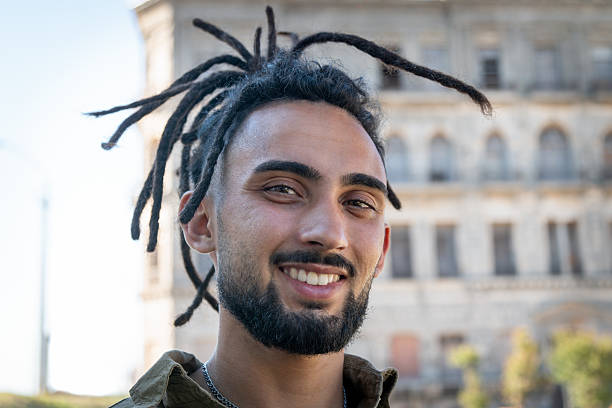Young man with dreadlocks smiling outdoors in an urban setting
