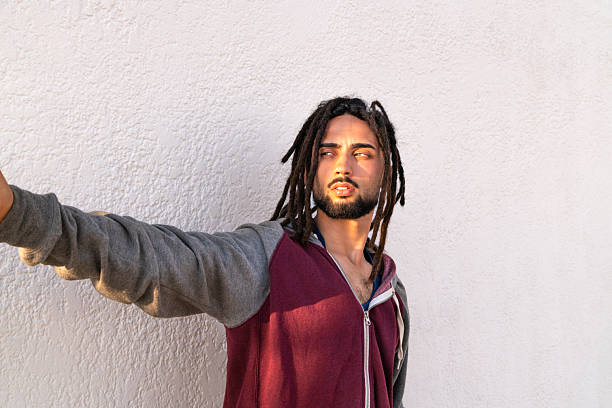 Young man with dreadlocks enjoying warm sun against a white wall