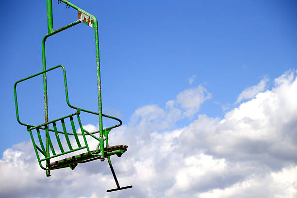 Empty green ski lift chair against a blue sky with clouds.
