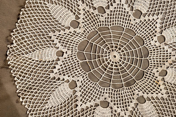 Handmade crochet lace doily closeup, radial circular floral pattern textile on table, vintage white cotton needlework, decorative home interior centerpiece, boho mandala ornament, top view, no people