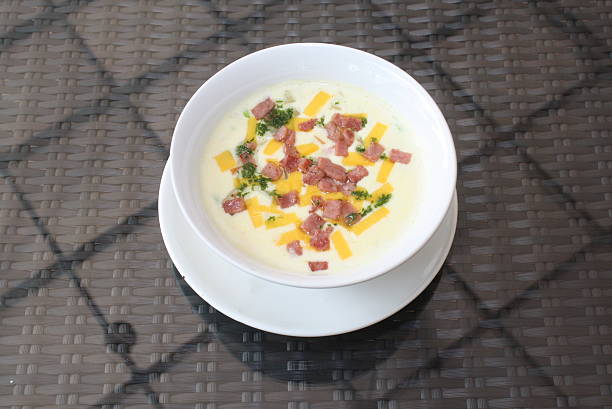 Hearty creamy soup topped with savory ham, sharp cheddar cheese, and fresh green parsley, served in a white bowl on a textured table