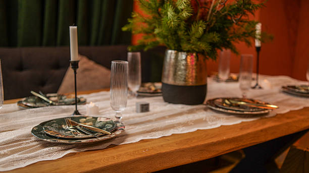 A beautifully arranged dining table awaits guests, featuring intricate floral plates, golden cutlery, tall candles, and a lush green centerpiece