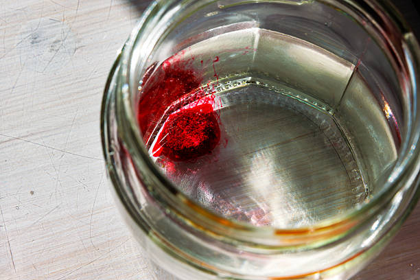 Top view into a glass jar of water with an red food dye tablet dissolving for easter egg dyeing