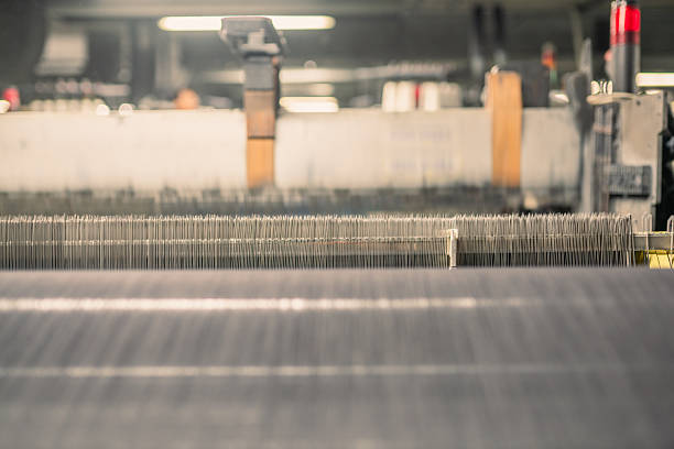 Close-up view of industrial textile machinery in a factory setting, showing the process of yarn and thread weaving for fabric production.
