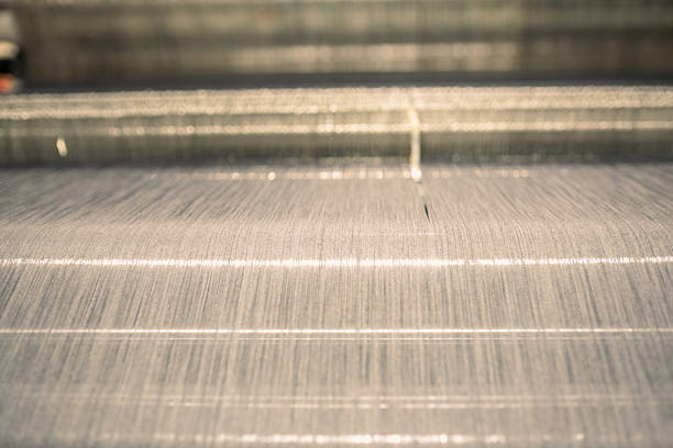Close-up view of industrial textile machinery in a factory setting, showing the process of yarn and thread weaving for fabric production.