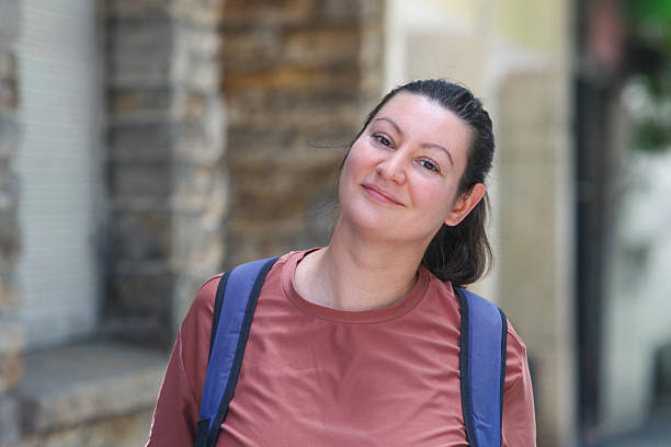 Portrait of a smiling adult woman wearing a backpack standing on an urban street in daylight.