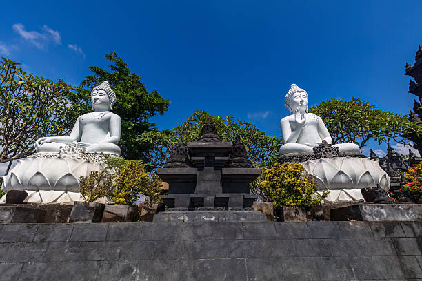 A pair of white Buddha statues at Brama Vihara Arama, a Buddhist temple and monastery in northern Bali, Indonesia. Deep blue sky overhead.