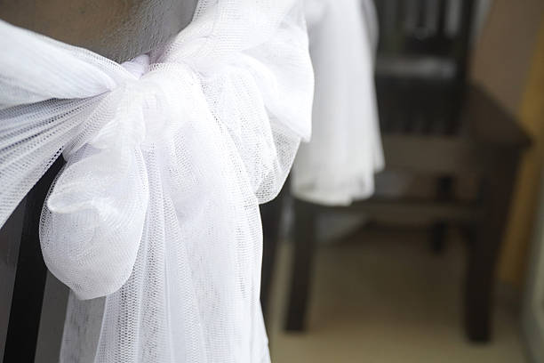 Charming white tulle bow adds elegance to a chair, perfect for wedding decor or special event styling. Refined and graceful touch.