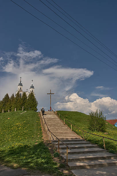 Stairway leading to a cross on a green hill with a church in the background and dramatic clouds in the sky. Concepts of faith, spiritual journey, hope and life choice.