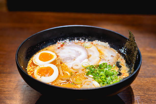 Delicious Japanese Tonkotsu ramen with soft-boiled egg and Chashu pork belly served in a black bowl on a wooden table. Hot, traditional Asian cuisine food concept.