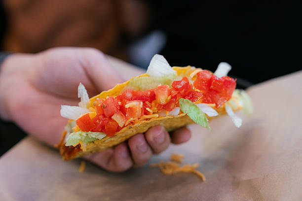 Hand Holding Fresh Taco with Tomato, Lettuce and Cheese