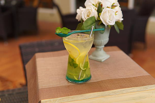 Refreshing cold beverage featuring lemon slices, fresh mint, and ice cubes, presented on a wooden table with a blurred floral background