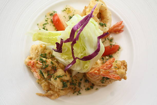 Elegant dish featuring crispy fried seafood, fresh green lettuce and red cabbage salad, and tomato slices, garnished with parsley